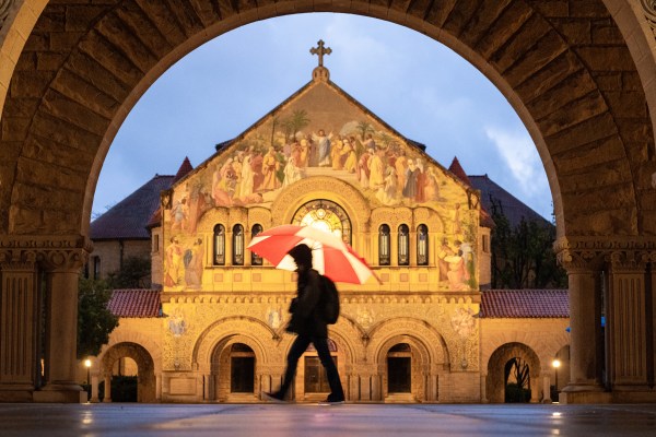 Person with red and white umbrella walks past Memorial Church at night during rain.
