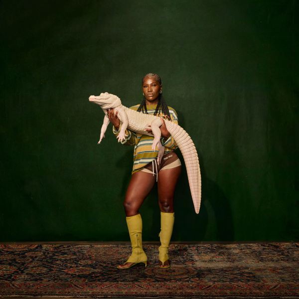 Hip hop artist Doechii stands against a green backdrop holding an albino alligator.